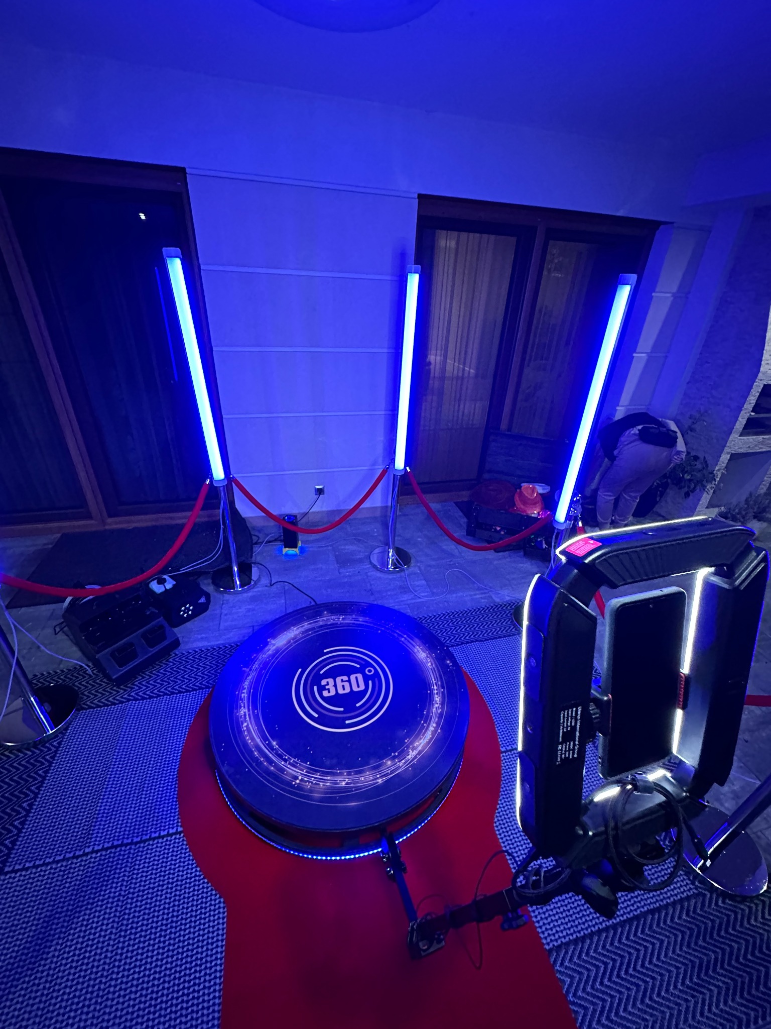Instalacja fotobudki 360 stopni z niebieskim oświetleniem LED, czerwonymi barierkami i widocznym sprzętem technicznym.