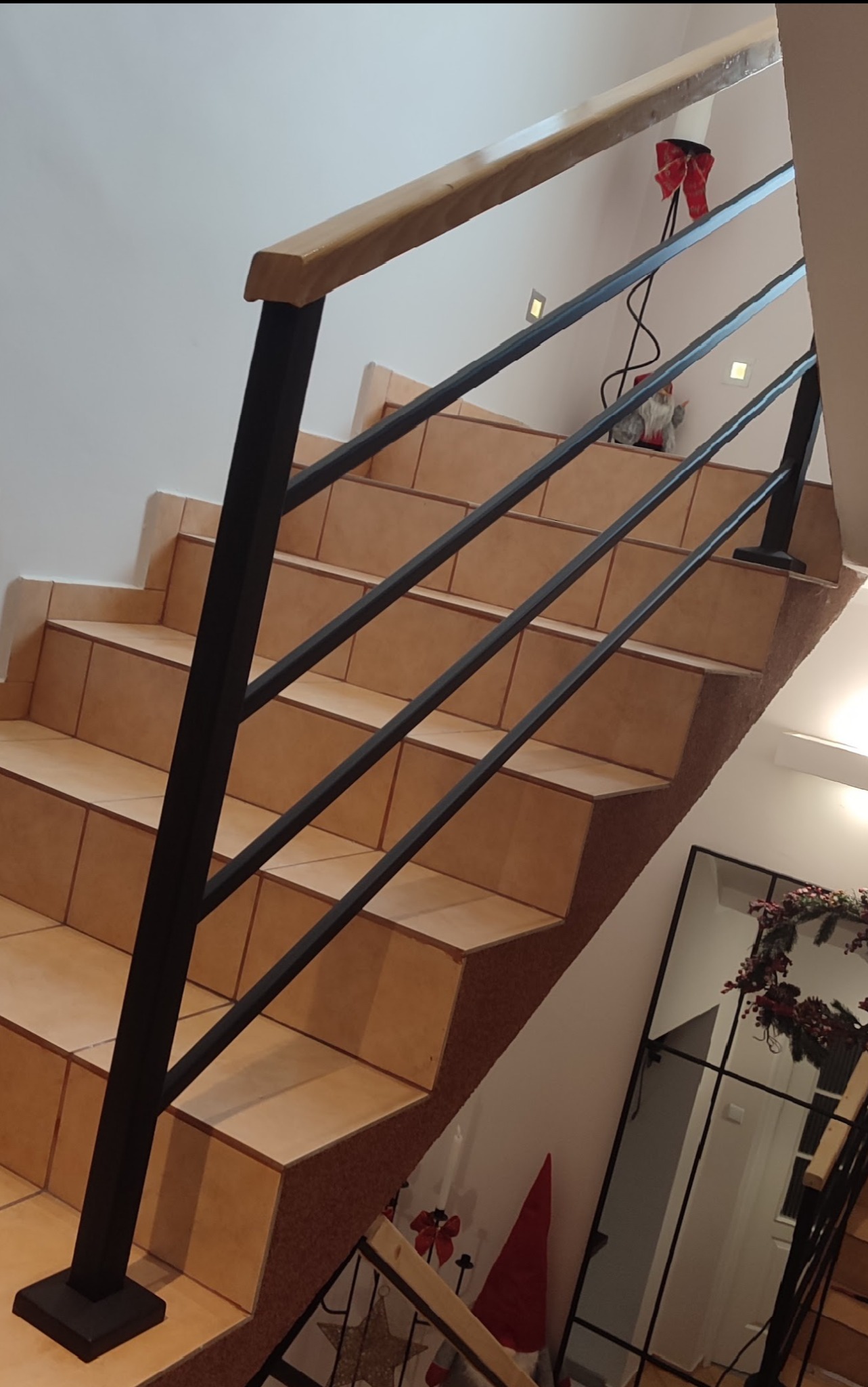 Schody wyłożone terakotą z czarną balustradą i drewnianym poręczem w domu w Jabłowie, widoczne świąteczne dekoracje i lustro.
