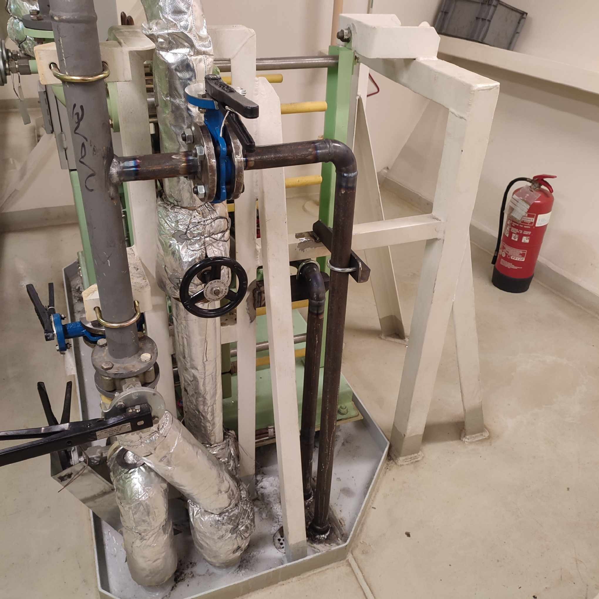 Instalacja przemysłowa z rurami, zaworami, izolacją termiczną i gaśnicą w tle, widoczne spawane łączenia rur.