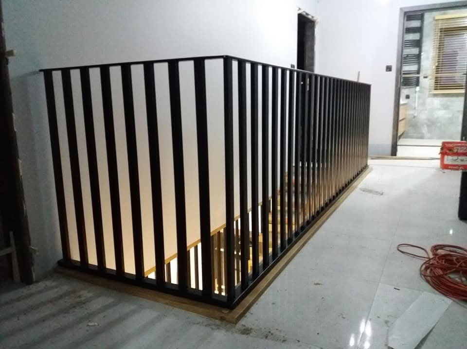 Nowoczesna balustrada schodowa z czarnych pionowych profili i białych paneli, zamontowana na drewnianej podstawie, widok z góry schodów, w tle fragment łazienki.