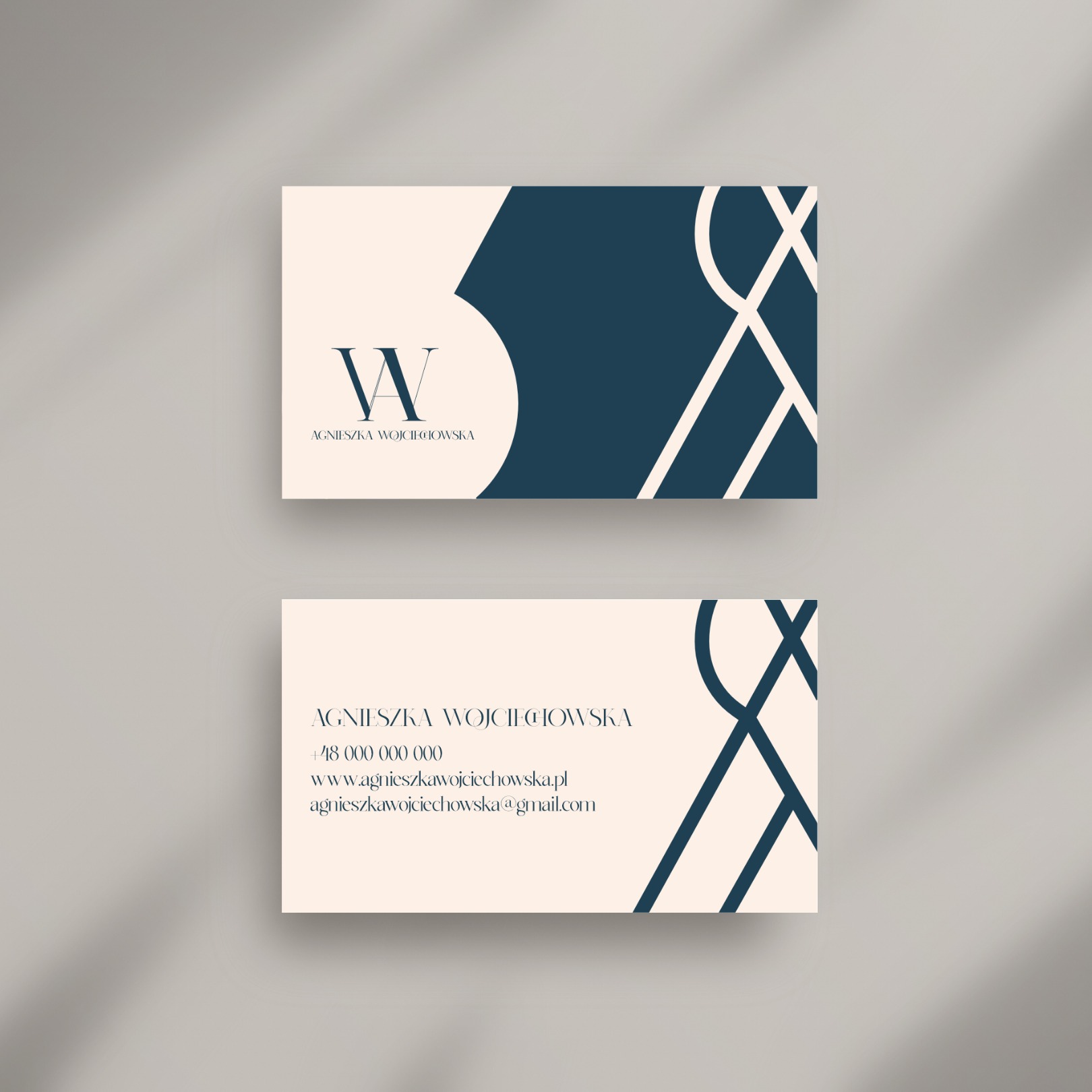 Dwie wizytówki z kremowym tłem i granatowym minimalistycznym logo oraz danymi kontaktowymi, ułożone na szarym tle z cieniem.