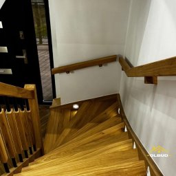OLBUD Bartosz Gliński - Drewniane schody kręcone z oświetleniem LED wzdłuż stopni i balustrad. Widok z góry, nowoczesne wykończenie, czarne elementy, białe ściany.