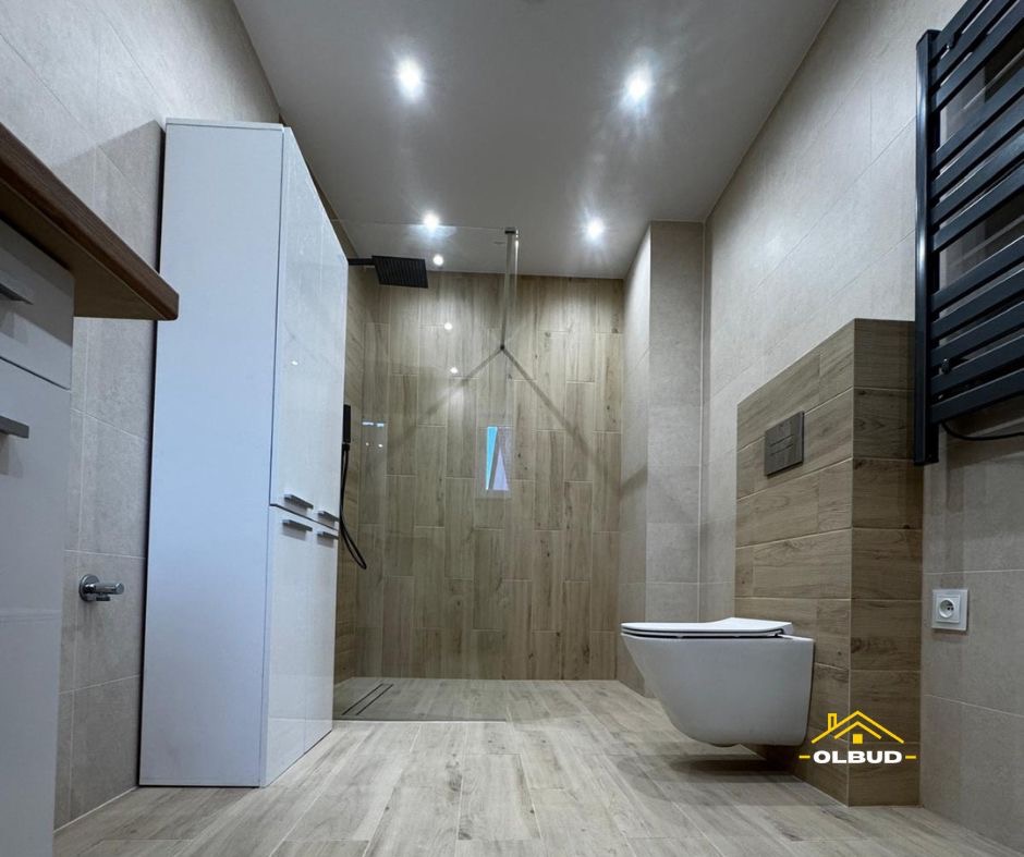 Nowoczesna łazienka z kabiną prysznicową typu walk-in, podwieszaną toaletą i grzejnikiem drabinkowym w kolorze czarnym. Płytki imitujące drewno na ścianach i podłodze.