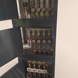 SUNOCO SPÓŁKA Z OGRANICZONĄ ODPOWIEDZIALNOŚCIĄ - Rozdzielacz ogrzewania podłogowego w szafce z otwartymi drzwiczkami, widoczne liczniki ciepła i zawory. Instalacja hydrauliczna w nowoczesnym budynku.