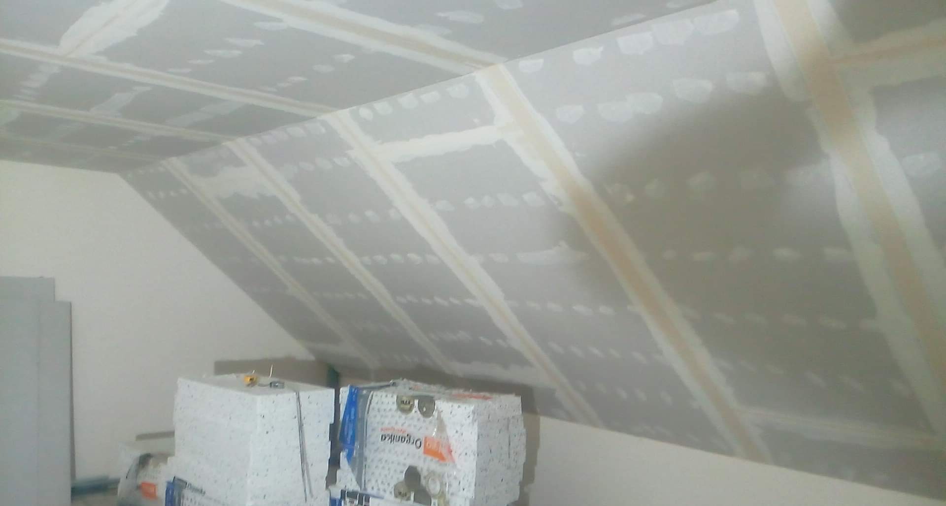 Poddasze z płyt kartonowo-gipsowych w trakcie szpachlowania, widoczne łączenia i przygotowane paczki płyt na podłodze.