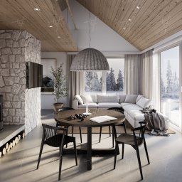 Molki Sp. z o.o. - Wnętrze domu w stylu skandynawskim z drewnianym sufitem, kamienną ścianą z kominkiem, okrągłym stołem z owocami, książką i świecą oraz widokiem na zaśnieżony krajobraz przez duże okna.