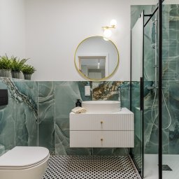 Molki Sp. z o.o. - Nowoczesna łazienka z turkusowymi płytkami imitującymi marmur, okrągłym lustrem w złotej ramie i kabiną prysznicową typu walk-in. Czarno-biała podłoga w geometryczny wzór.
