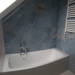 Luxury House - Wanna w łazience na poddaszu z błękitnymi płytkami imitującymi marmur. Grzejnik drabinkowy na ścianie. Bateria wannowa chromowana. Całość utrzymana w chłodnej tonacji.