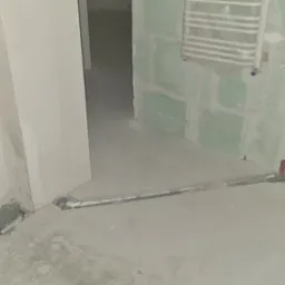 Wnętrze łazienki w trakcie remontu: zamontowany stelaż podtynkowy WC Cersanit Tech Line, widoczne rury kanalizacyjne w bruzdach w posadzce, przygotowane przyłącza wodne na ścianie. Ściany częściowo...