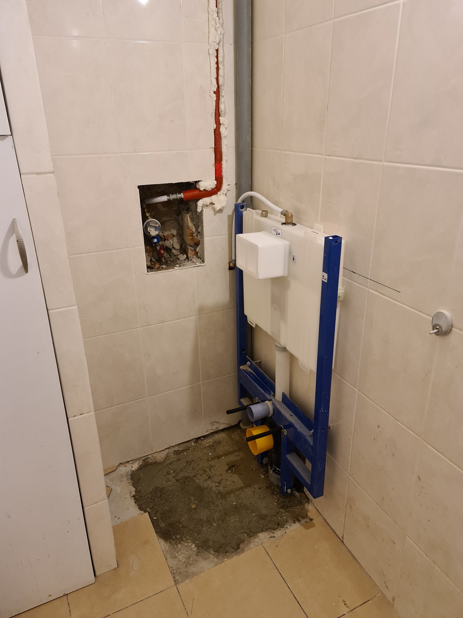 Świeżo zamontowany stelaż podtynkowy WC na tle beżowych płytek, widoczne przyłącza wodne i kanalizacyjne, oraz fragment instalacji wodnej w ścianie zabezpieczonej pianką montażową.