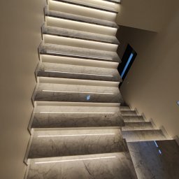 F.U. COMPLEX CONSTRUCTION WOJCIECH WOŹNIAK - Schody wewnętrzne wykończone marmurem, podświetlone listwami LED, widok z góry na dół.