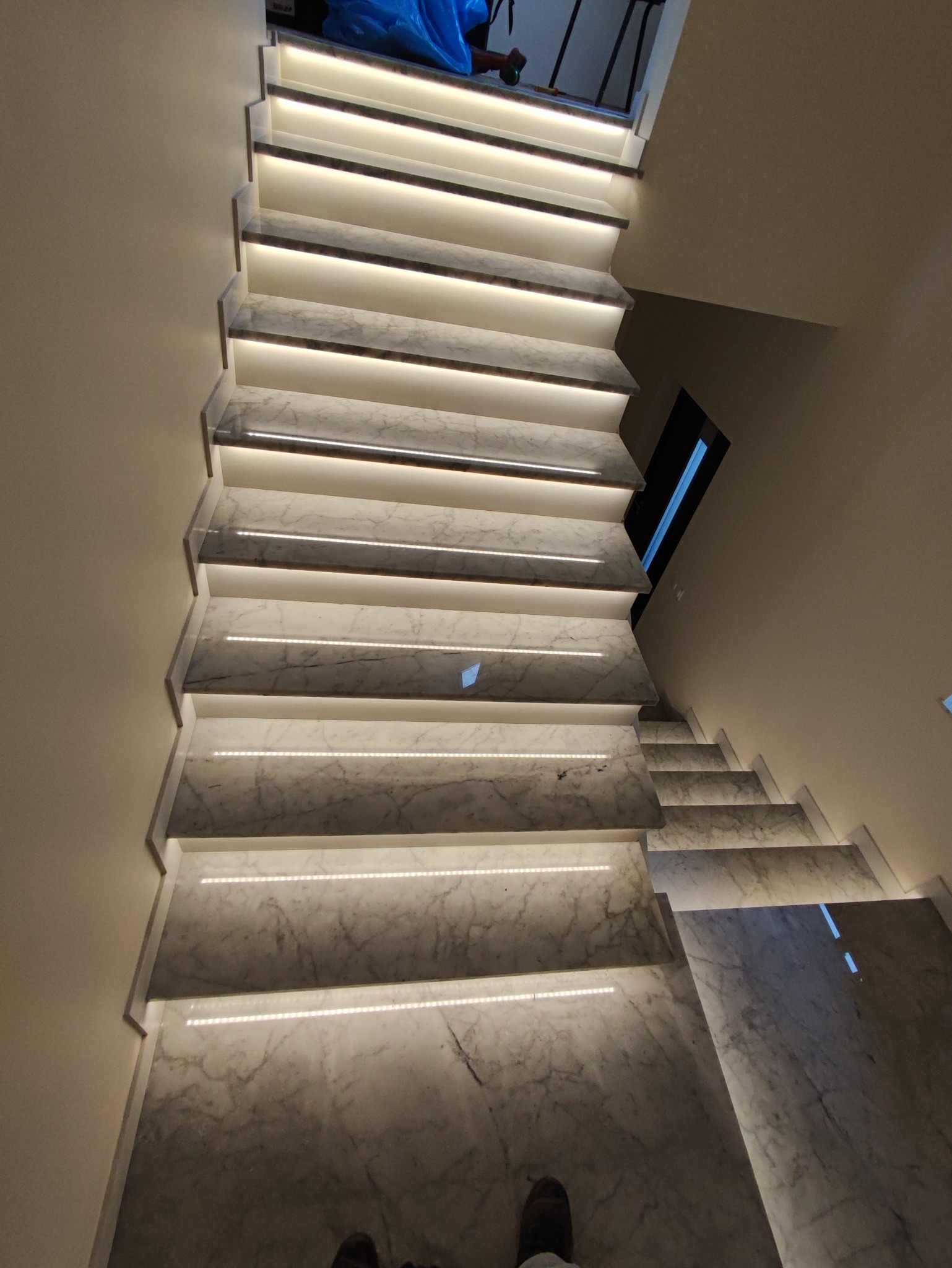 Schody wewnętrzne wykończone marmurem, podświetlone listwami LED, widok z góry na dół.