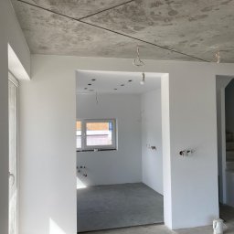 Fix PDP - Surowy betonowy sufit i świeżo pomalowane na biało ściany w nowym mieszkaniu w Krakowie, widoczne instalacje elektryczne i hydrauliczne, przygotowane pod dalsze prace wykończeniowe.