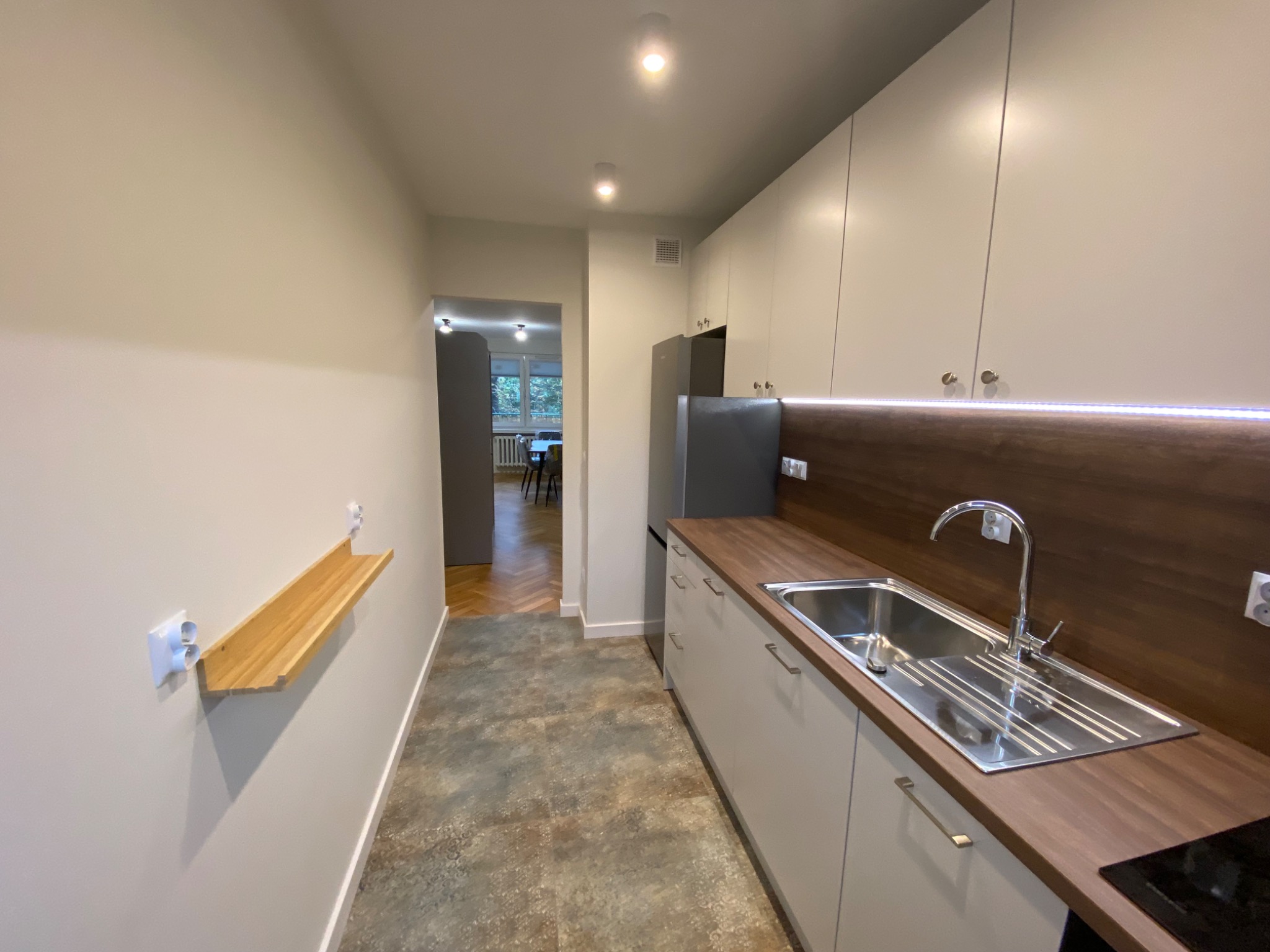 Nowoczesna kuchnia z szarymi szafkami, drewnianym blatem i panelem, stalowym zlewem, oryginalną podłogą i widokiem na jadalnię z parkietem w jodełkę.