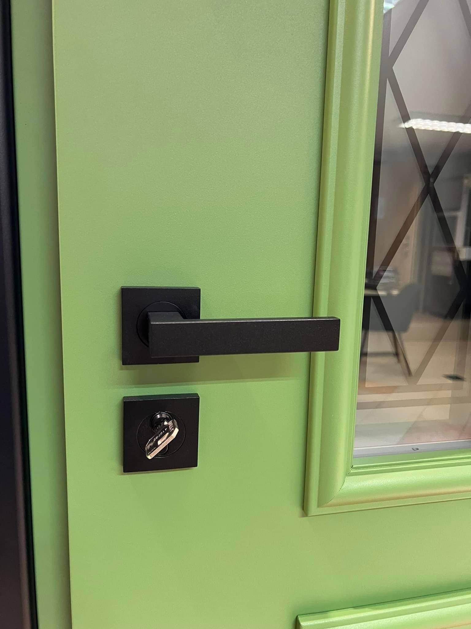 Jasnozielone drzwi z czarną klamką i szybą z geometrycznym wzorem, prezentowane w Rzeszowie.