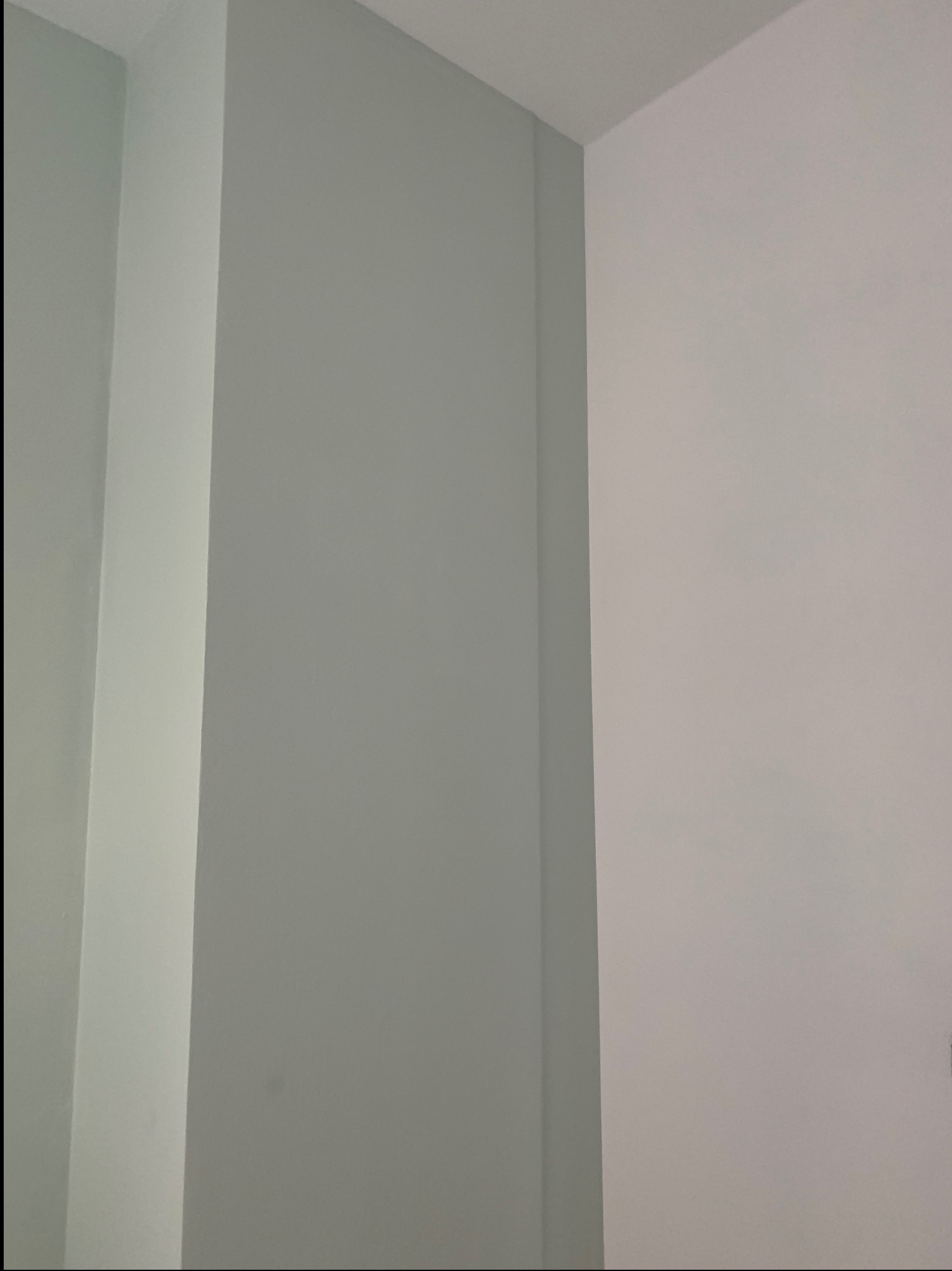 Pomieszczenie po malowaniu, widoczny róg pokoju, ściany w odcieniach szarości i bieli, z delikatnym światłocieniem.