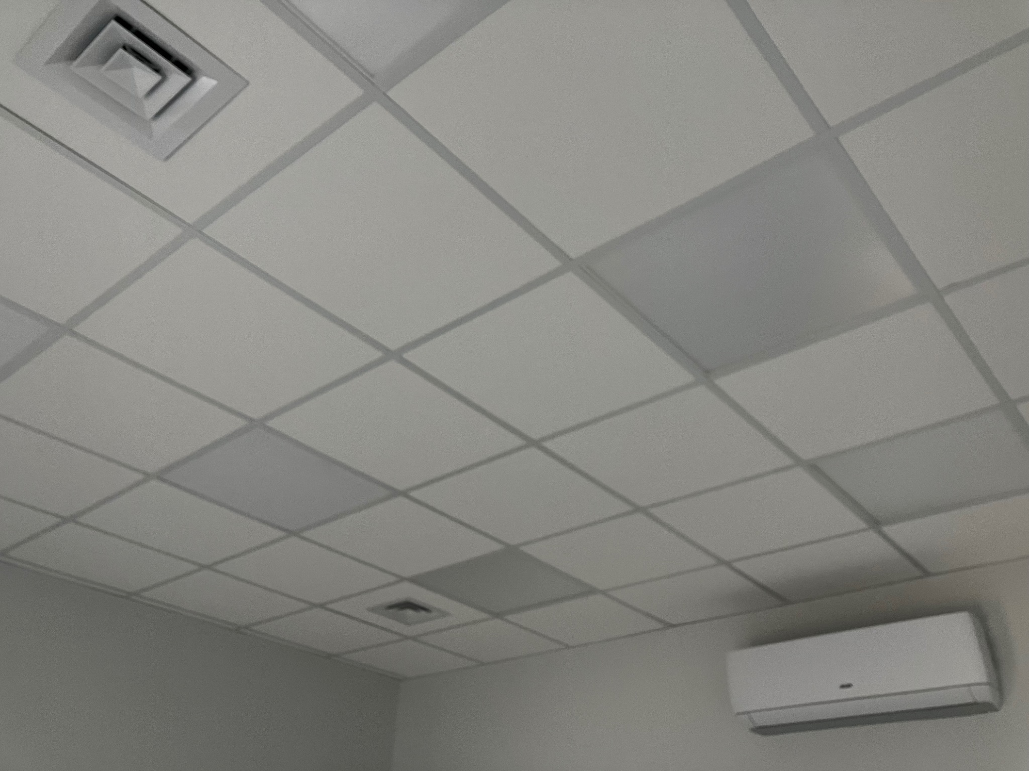 Kasetonowy sufit z kratką, widoczny anemostat i klimatyzator ścienny w pomieszczeniu biurowym.