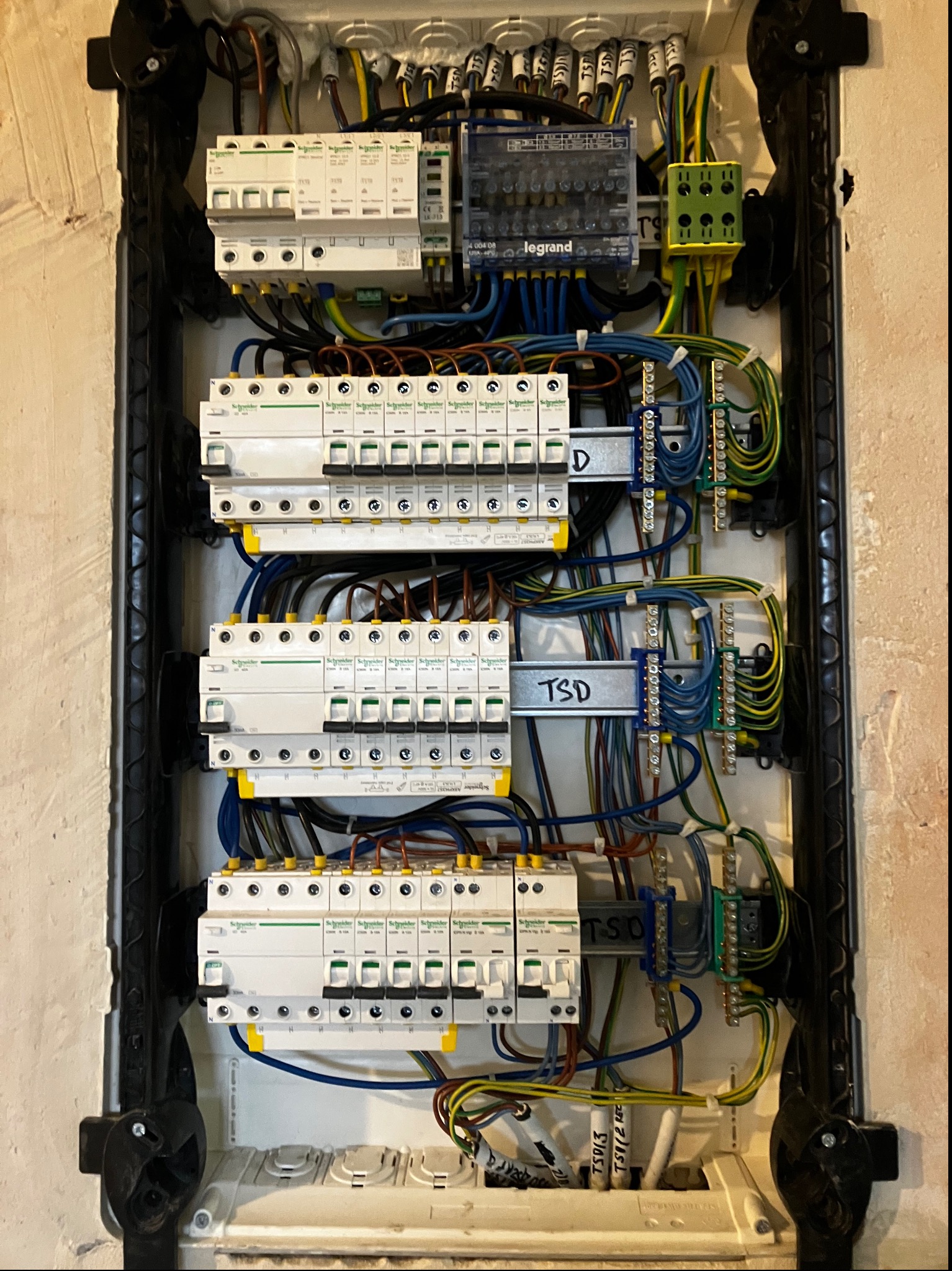 Otwarta skrzynka elektryczna z widocznymi bezpiecznikami, przewodami i złączkami, zamontowana na ścianie o nierównej fakturze.