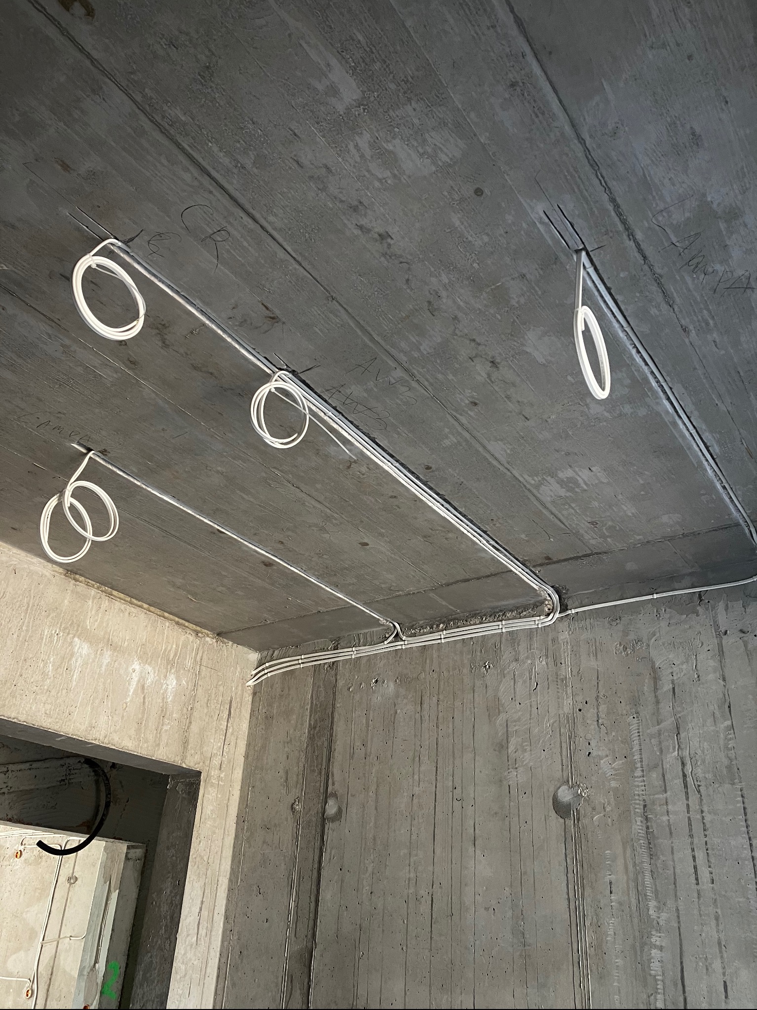 Surowe wnętrze w trakcie prac: widoczne kable elektryczne prowadzone po betonowym suficie i ścianach, z charakterystycznymi pętlami kabli na suficie, podkreślające etap instalacji.