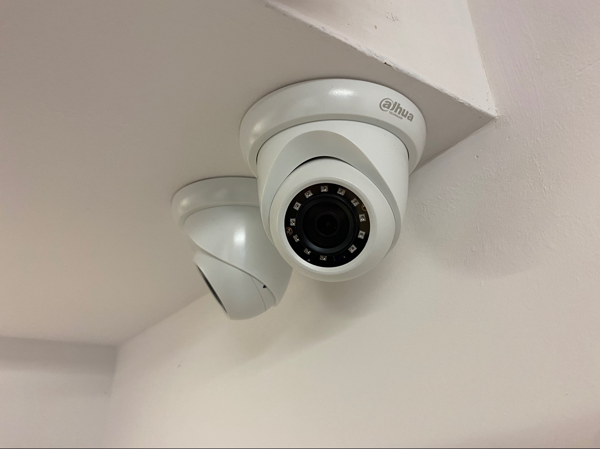 Dwie białe kamery monitoringu Dahua zamontowane pod sufitem w rogu pomieszczenia, widok od dołu.