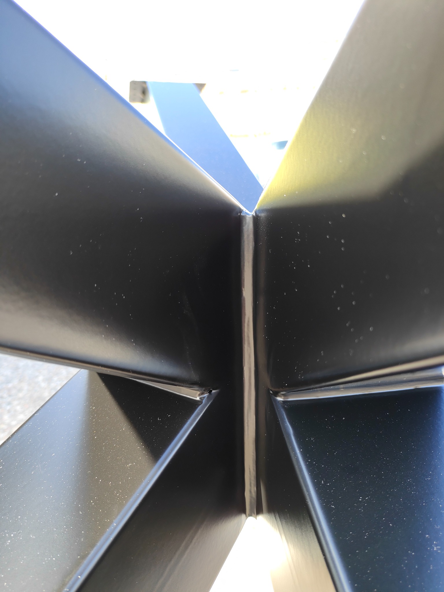 Szczegółowy widok spawu łączącego cztery metalowe profile pomalowane na czarno, widoczne drobne niedoskonałości na powierzchni.