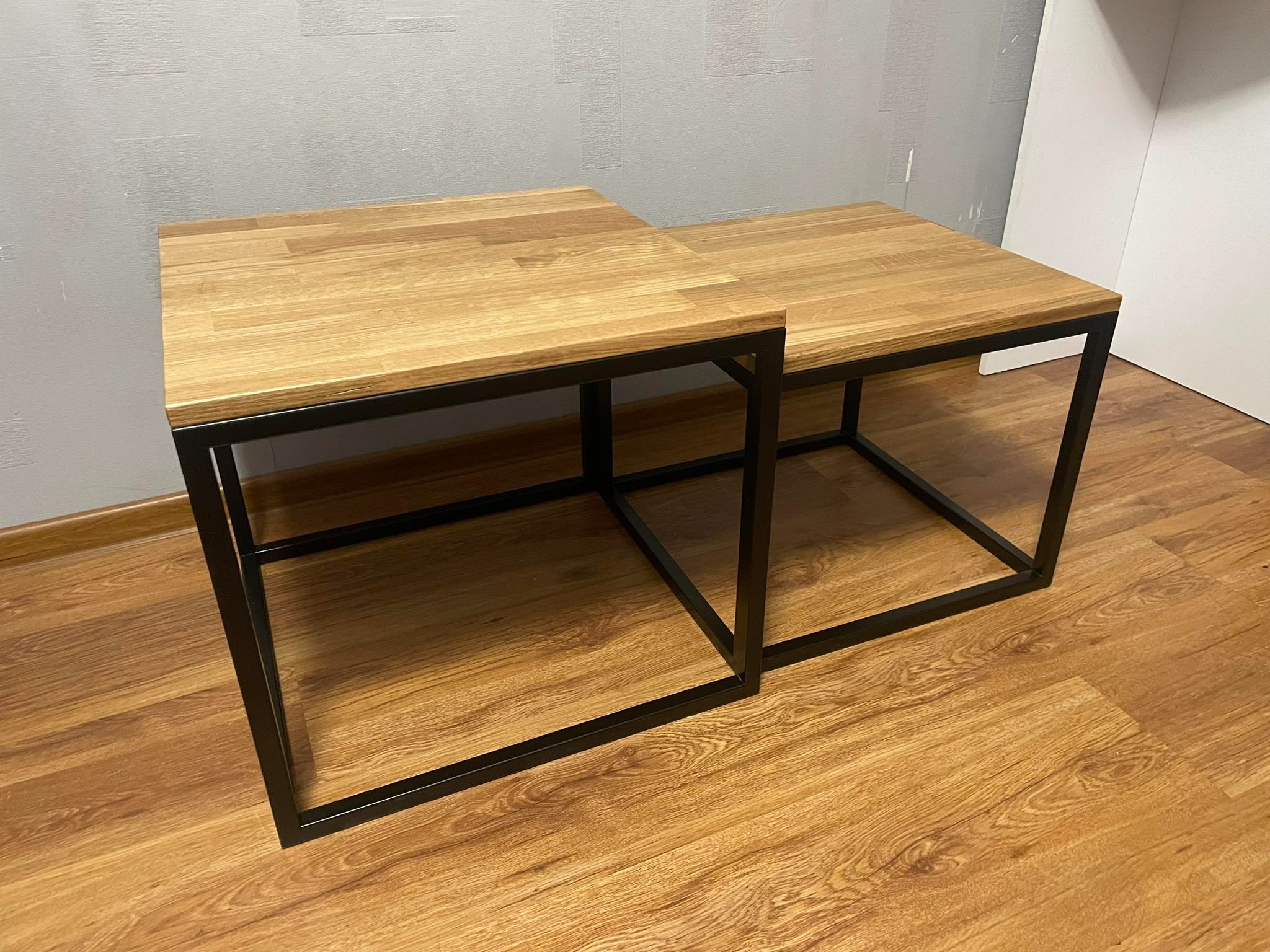 Dwa stoliki kawowe z drewnianymi blatami i czarnymi, metalowymi ramami, ustawione jeden w drugim na podłodze z paneli.