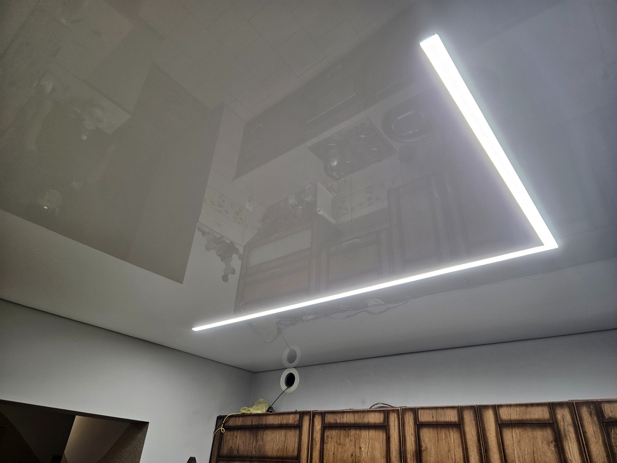 Błyszczący sufit z odbiciem wyposażenia kuchni i trójkątnym oświetleniem LED, widoczne okablowanie i otwory wentylacyjne.