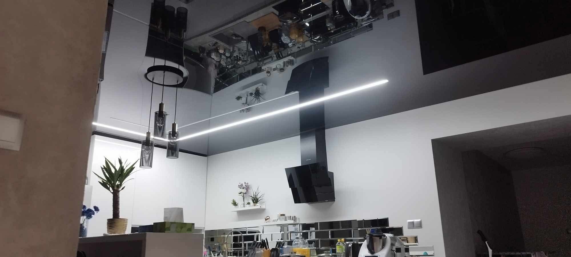 Nowoczesna kuchnia z czarnym, błyszczącym sufitem z oświetleniem LED, wiszącymi lampami i czarnym okapem na białej ścianie z płytkami lustrzanymi.