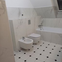 Piotr Korbel Vertikor - Nowoczesna łazienka na poddaszu z biało-czarną podłogą w karo, białe płytki imitujące marmur na ścianach, wisząca toaleta i bidet oraz wanna z chromowaną armaturą.
