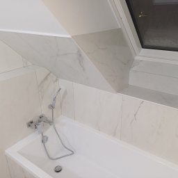 Piotr Korbel Vertikor - Nowoczesna łazienka na poddaszu z białą wanną, chromowaną baterią i kabiną prysznicową oraz marmurowymi płytkami ułożonymi pod skosem, oświetlona przez okno dachowe.