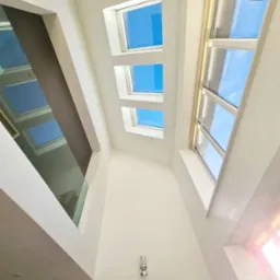 Wysokie wnętrze z trzema oknami dachowymi, dużym oknem bocznym i szklaną balustradą, pomalowane na biało, widok z dołu.