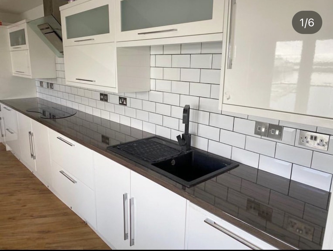 Nowoczesna kuchnia z białymi szafkami na wysoki połysk, ciemnym blatem, czarnym zlewem i białą glazurą ułożoną w cegiełkę z czarną fugą.