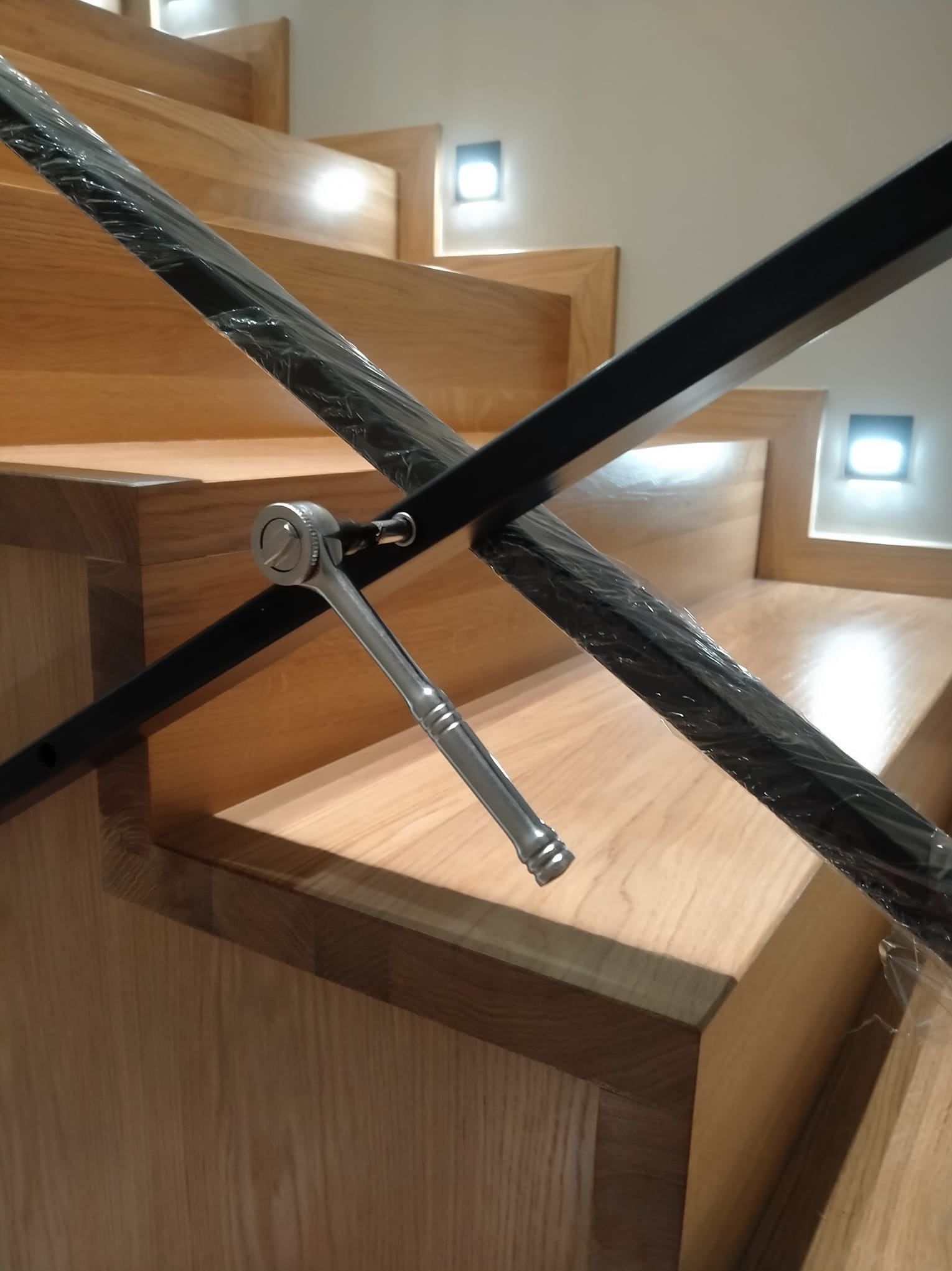 Montaż czarnej balustrady schodowej z drewna dębowego. Na schodach widoczny klucz nasadowy, używany podczas instalacji. Balustrada zabezpieczona folią.