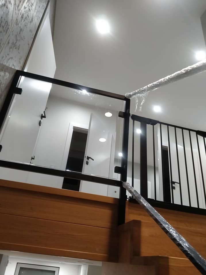 Nowoczesna balustrada ze szkła i czarnego metalu, zabezpieczona folią ochronną po montażu, widok od dołu, jasne wnętrze.