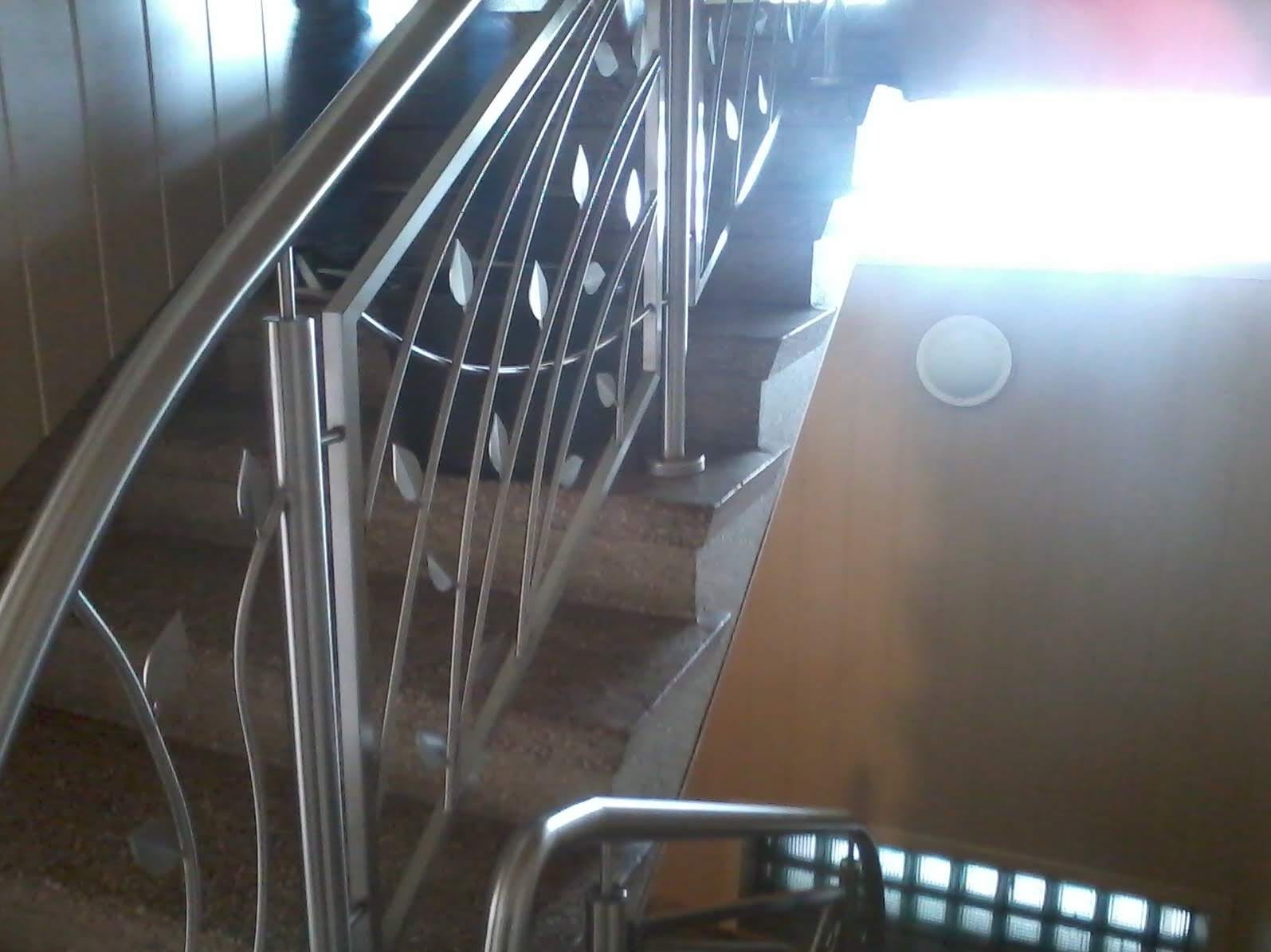 Schody z balustradą ze stali nierdzewnej, dekorowane motywem liści. Widok z dołu, oświetlenie od góry.