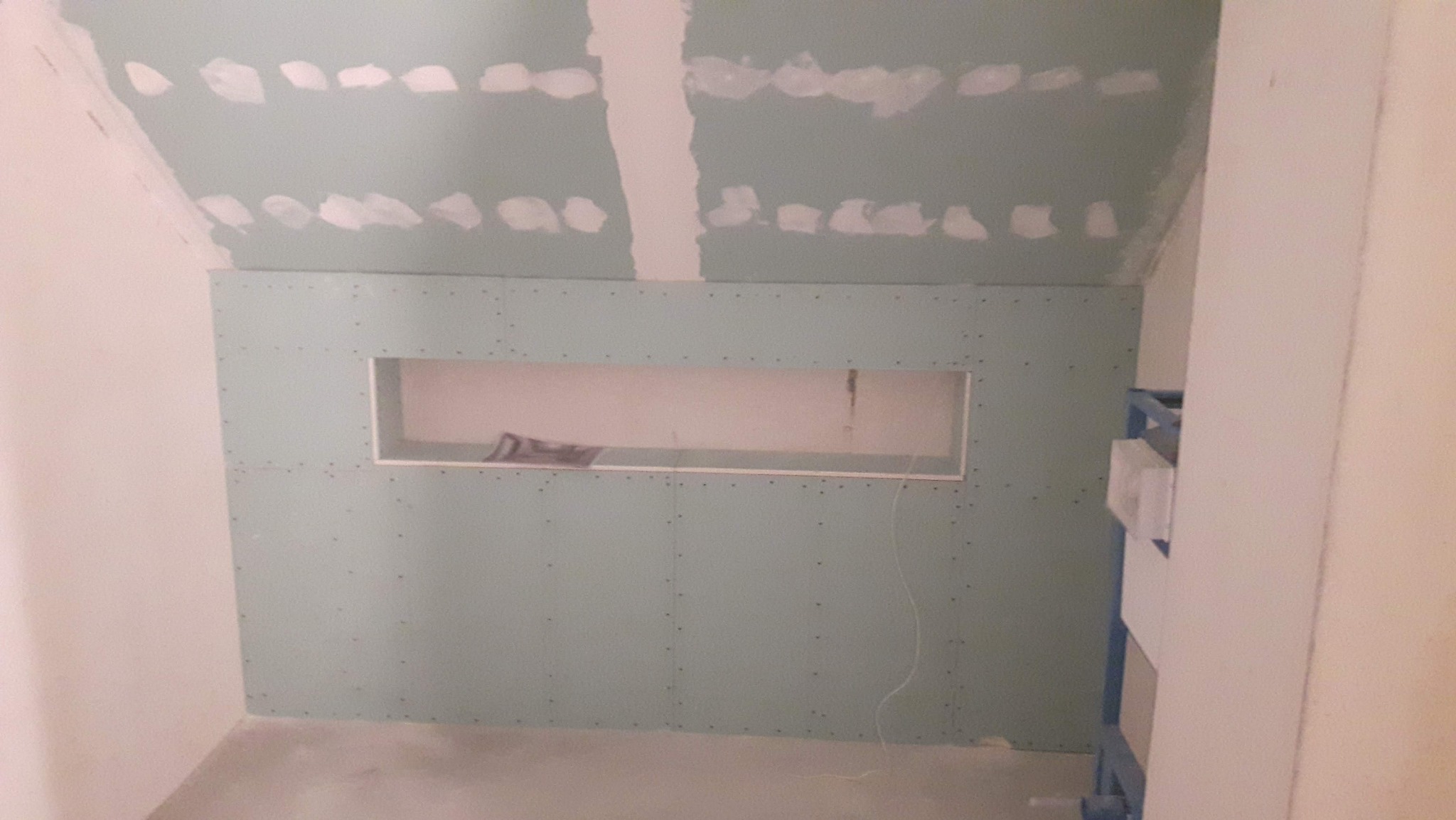 Ściana z płyty gipsowo-kartonowej z otworem w skosie poddasza, widoczne łączenia płyt i szpachlowanie. Etap prac wykończeniowych w pomieszczeniu.