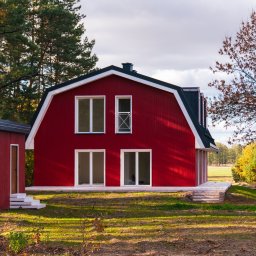 Anna Matus - Agent Nieruchomości - Czerwony dom w stylu stodoły z białymi oknami i czarnym dachem, otoczony drzewami w jesiennej scenerii.
