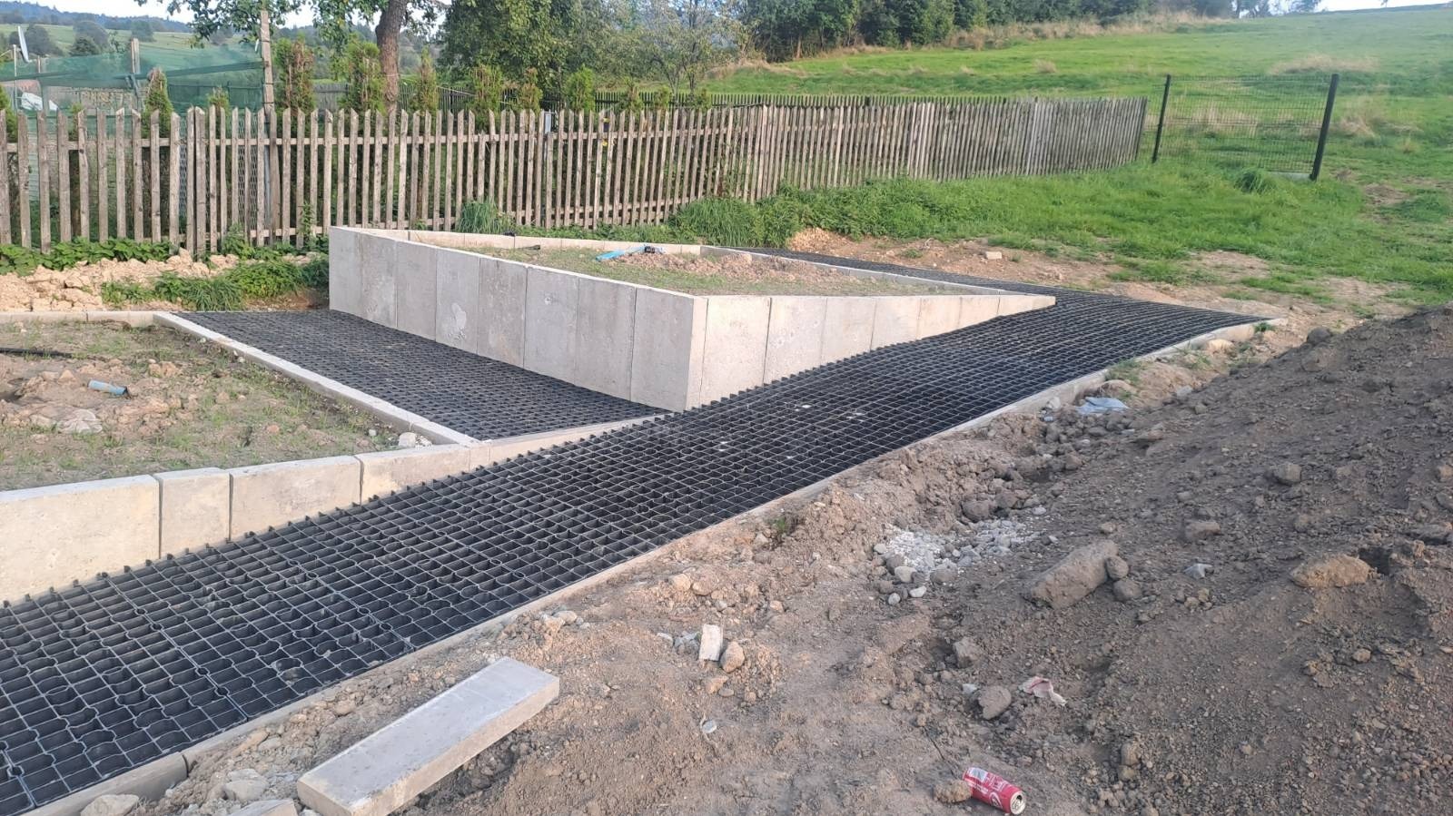 Przygotowanie podłoża pod nawierzchnię z ażurowych płyt w Kątach Węgierskich, widoczne betonowe obrzeża i fragment ogrodzenia w tle.