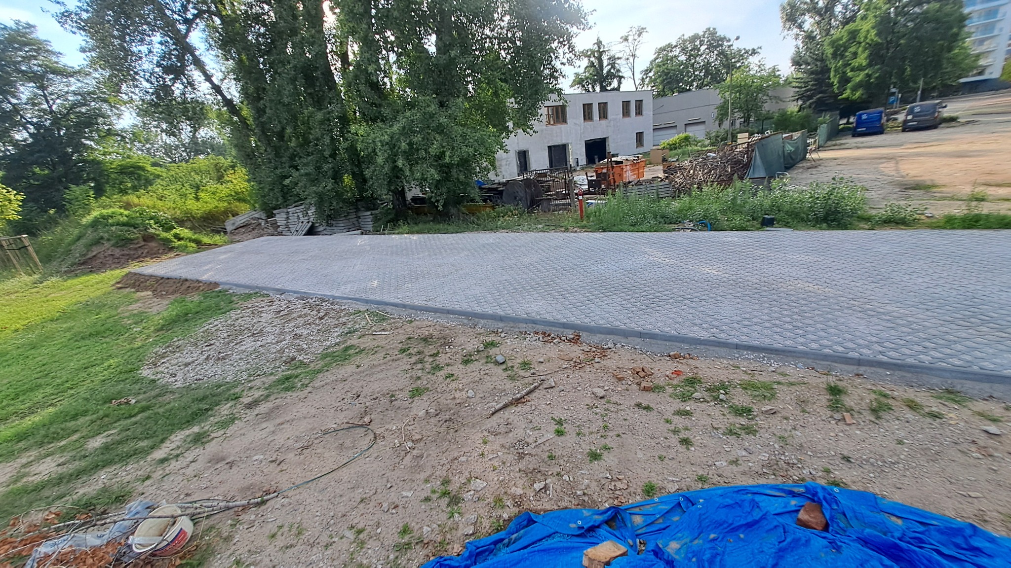 Nowa, szara kostka brukowa ułożona na podjeździe, z widocznym obrzeżem. W tle budynek i zieleń. Ujęcie z dołu, podkreślające regularny wzór kostki.