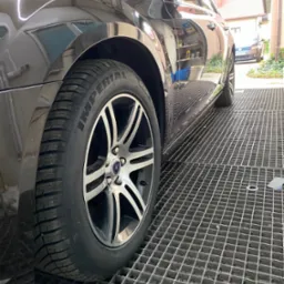 Błyszczący, ciemny samochód na metalowej kratownicy, widoczny bieżnik opony Imperial i felga z wieloma ramionami, odbicie otoczenia w lakierze.