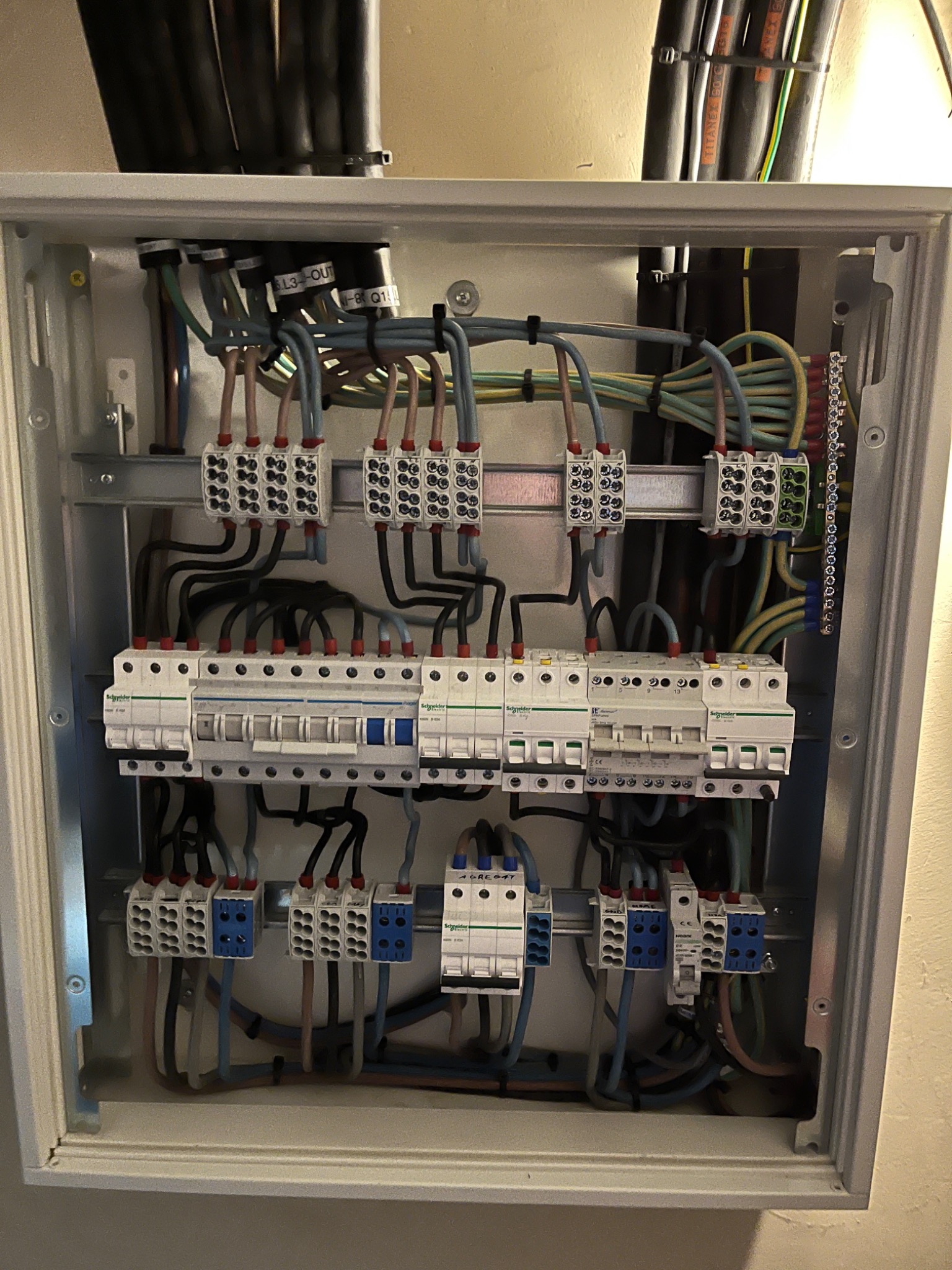 Otwarta skrzynka elektryczna z widocznymi bezpiecznikami, przewodami o różnych kolorach i złączkami, zamontowana na ścianie.