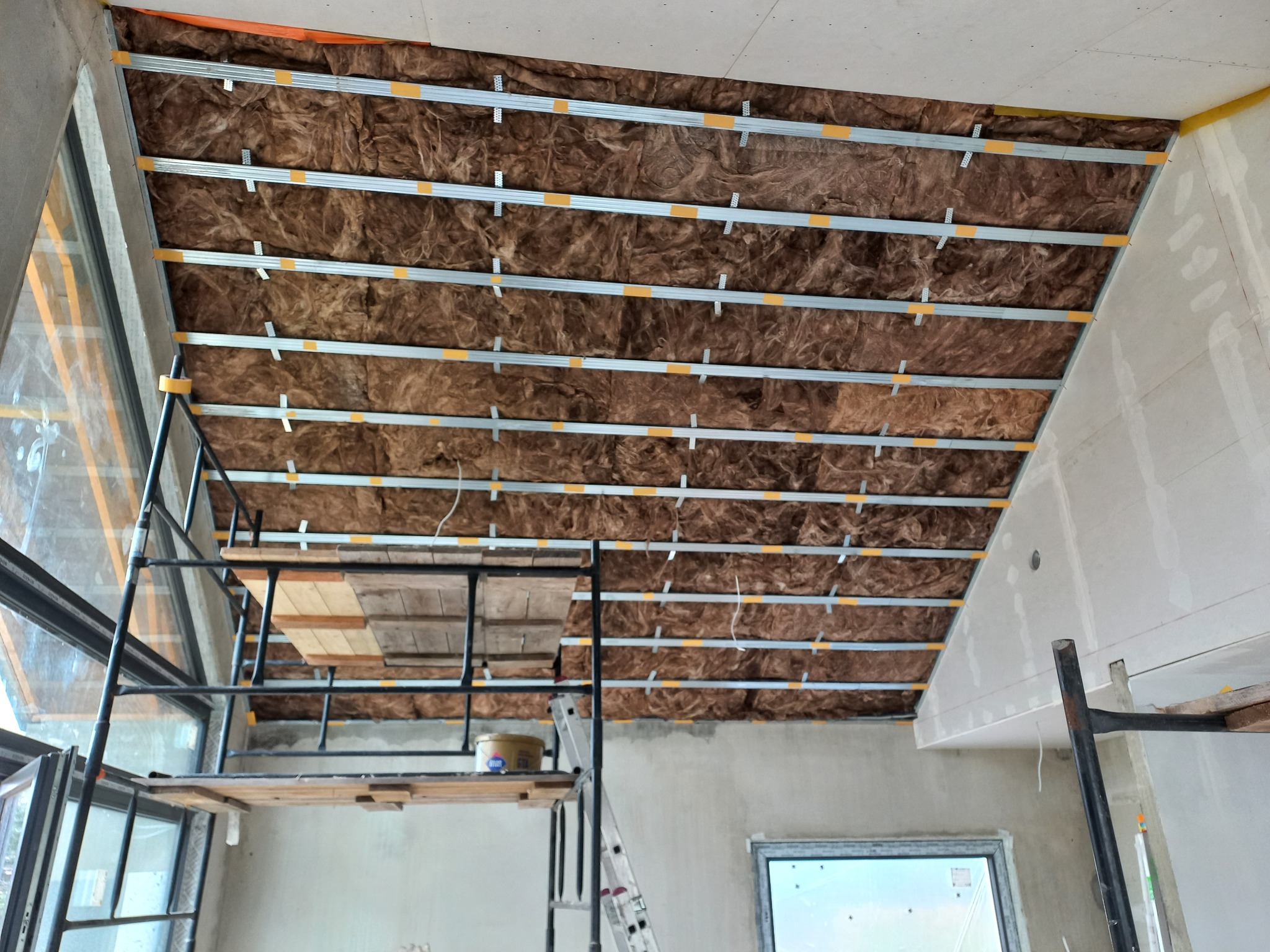 Montaż izolacji z wełny mineralnej na poddaszu w Łodzi, widoczne metalowe profile mocujące i rusztowanie.