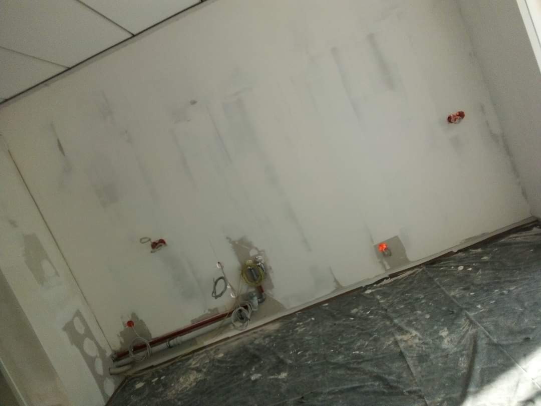 Pokój w trakcie szpachlowania ścian, widoczne instalacje elektryczne i rury, podłoga zabezpieczona folią malarską.