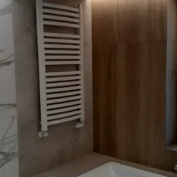 Nowoczesna łazienka z wanną obudowaną szarą płytką, drewnianą ścianą i białym grzejnikiem drabinkowym, oświetlona listwą LED pod sufitem.