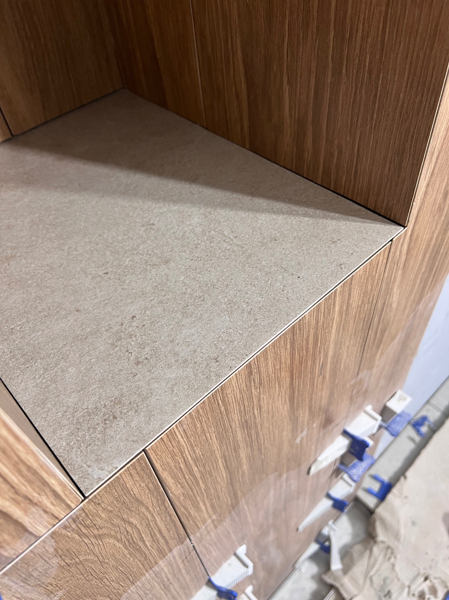 Półka z płytek imitujących drewno, beżowa płytka na górze, widoczne klipsy poziomujące, zbliżenie.