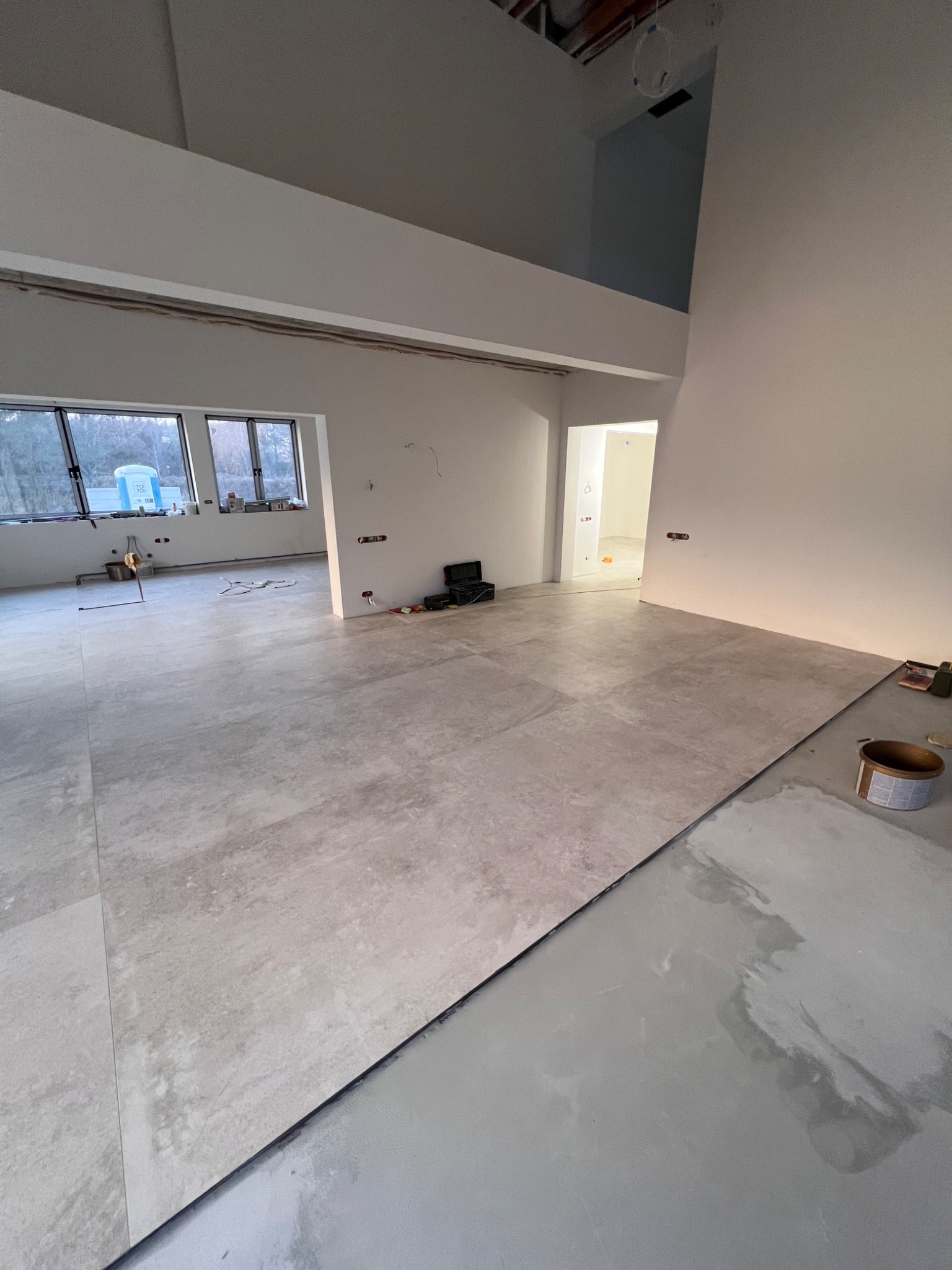 Układanie płytek podłogowych w przestronnym, jasnym wnętrzu w Warszawie, widoczne narzędzia glazurnicze i częściowo wykończona podłoga.