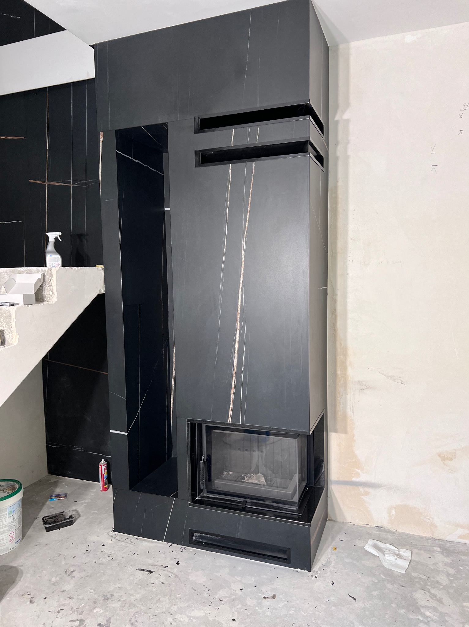 Montaż obudowy kominka z czarnych płyt imitujących marmur z jasnymi żyłami w trakcie prac wykończeniowych w Warszawie.