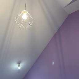 Komfort Bud - Lampa wisząca w stylu geometrycznym, sufit skośny biały, ściana fioletowa z refleksami światła.
