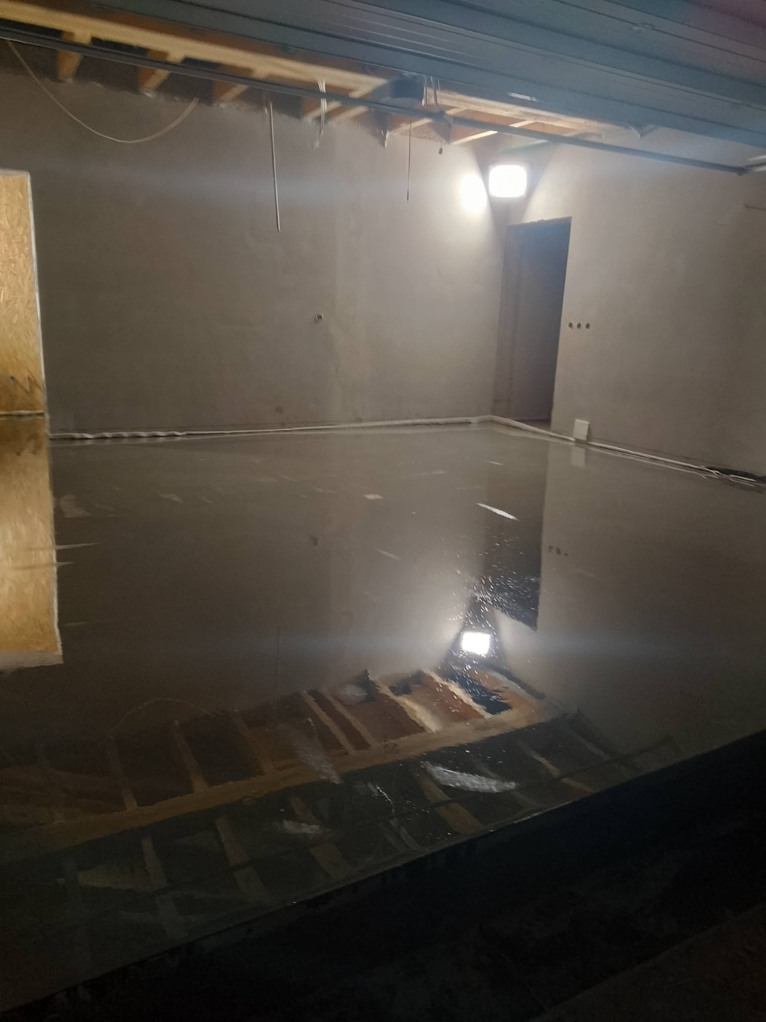 Wylana, mokra posadzka w pomieszczeniu ze ścianami w szarym kolorze, widok z dołu, Zblewo. Widoczne elementy instalacji podłogowej.