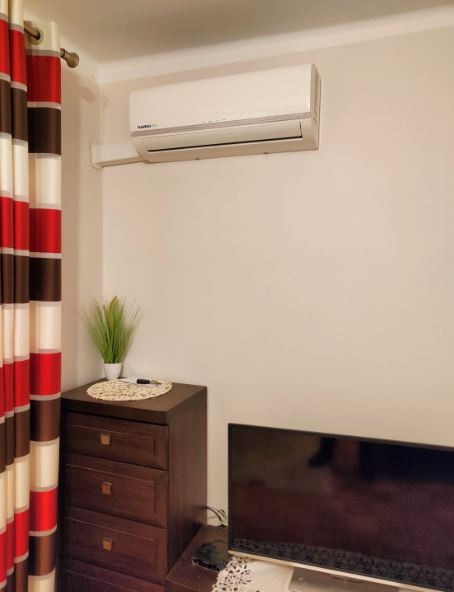 Biała jednostka klimatyzacji ściennej zamontowana w pokoju z ciemnymi meblami i zasłonami w paski.
